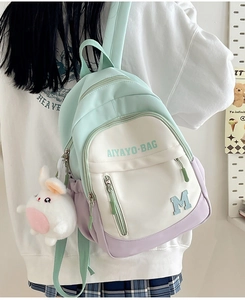 Side view of a mint green and lavender nylon backpack with a plush bunny charm on a model