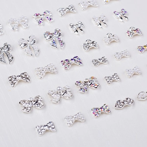 Detailed macro view of silver bow-shaped nail charms with pearls and sparkling rhinestones