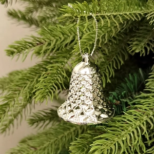 Nahaufnahme silberner, ausgehöhlter Weihnachtsklingeln vor festlichen grünen Tannenzweigen