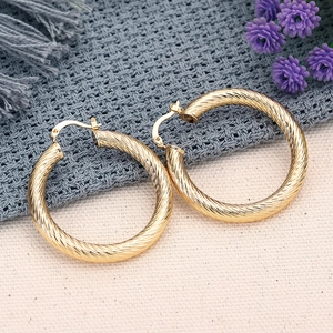 Macro di grandi orecchini a cerchio dorati con trama a spirale e chiusura a scatto