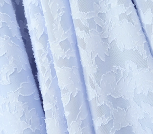 Detailed macro view of light blue fabric with textured floral jacquard and embroidery