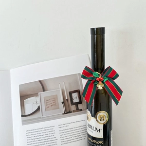 Close-up of red and green striped Christmas bow with gold bells on a wine bottle