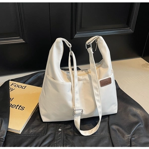 Detail of white nylon tote bag with brown leather logo patch and adjustable strap