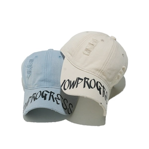 Detailed macro view of distressed cotton baseball caps with NOW PROGRESS printed on the brim