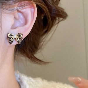 Close-up of bow knot stud earring with black gold contrast and clear zircon on ear