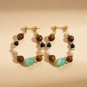 Detail of beaded hoop earrings with tiger eye, pearls, and gold accents on paper
