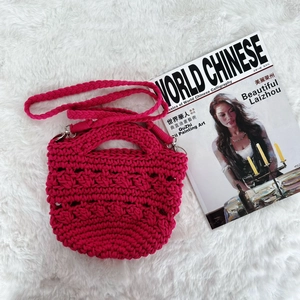 Detail of rose red crochet handbag with curved handle and detachable woven shoulder strap