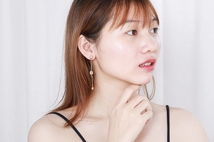 Long gold tassel earrings with oval beads worn by a model against a white background