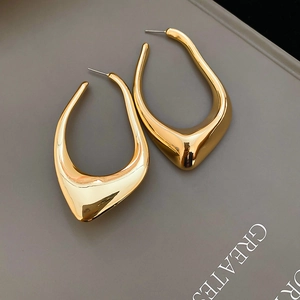 Macro shot of sculptural gold irregular hollow earrings on a clean grey background