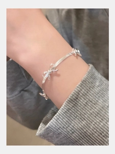Silver bow knot snake chain bracelet on female wrist with grey knit sleeve detail