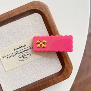 Pince à cheveux rose à bords ondulés avec nœud doré sur plateau à bijoux en bois