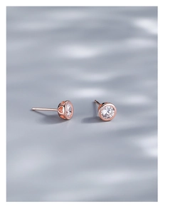 Detail of rose gold stud earrings featuring a clear round stone and heart cutout sides