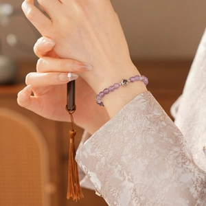 Detail of purple amethyst bead bracelet with silver hollow charm and silk tassel accessory