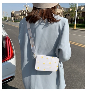 Detail of white crossbody bag featuring blue and yellow daisy prints and a wide strap