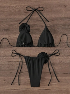Flat lay of black bikini with 3D floral appliques on a dark wooden background
