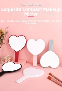 Detailed view of heart-shaped handheld makeup mirrors in multiple colors on a pink background