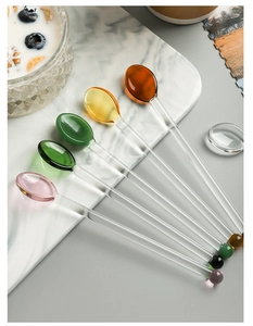 Set of six colorful glass stirring spoons with heart-shaped beads on a marble tray