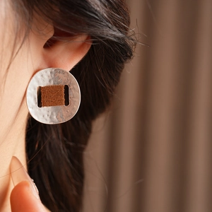 Dettaglio dell'orecchino tondo martellato argento con inserto in tessuto marrone