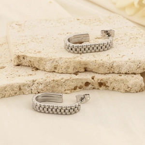 Detailed view of silver U-shaped earrings with gear-like texture on beige stone