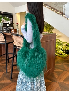 Detail of green faux fur heart-shaped bag with tassels shown on a shoulder in a cafe