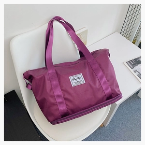 Detailansicht der lila Oxford-Reisetasche mit Markenlabel auf einem weißen Designerstuhl