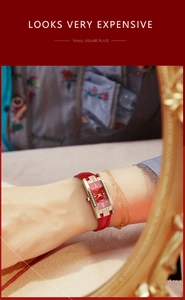 Detail of red leather strap and gold square watch case with diamond accents and red dial