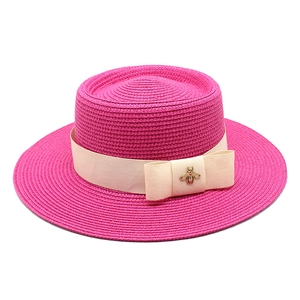 Detail view of woven straw hat featuring a chic gold bee ornament and cream ribbon decoration