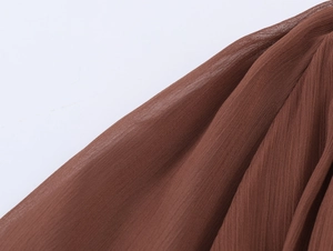 Detailed macro view of dark brown pleated chiffon fabric texture on a bohemian dress