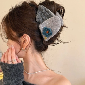 Gros plan d'une pince à cheveux en tricot gris ornée d'une petite fleur bleue
