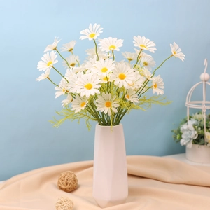 Close-up of white artificial daisies in a white geometric ceramic vase on blue background