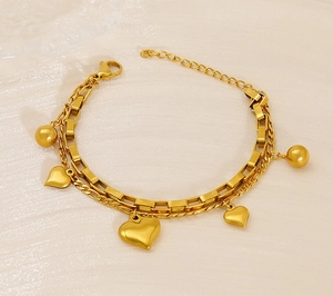 Détail d'un bracelet double couche doré avec pendentifs en cœur et fermoir mousqueton