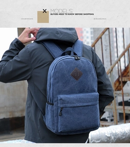 Rear view of a navy blue canvas backpack featuring a leather diamond patch and zipper pocket