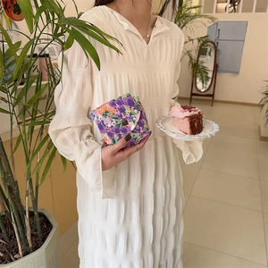 Close-up of floral mini storage pouch with button closure held against a white dress