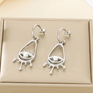 Détail de boucles d'oreilles argentées avec motif œil et perle blanche sur boîte