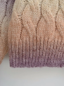 Detail of cable knit pattern on soft gradient sweater transitioning from beige to purple