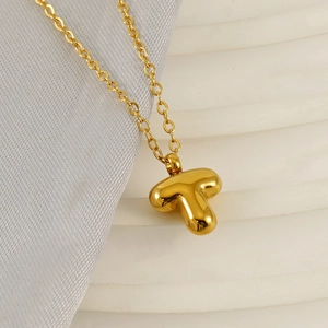 Polished gold bubble letter T pendant necklace on a minimalist silk background