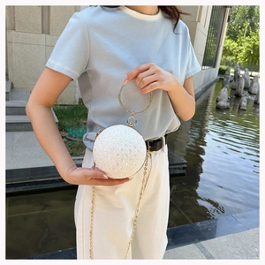 Detail of white spherical evening bag with pearl texture and golden handle on a model