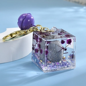Detail of cube resin keychain with Together pebble, purple flowers and gold bell