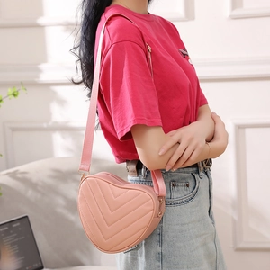 Pink heart-shaped crossbody bag with V-stitch quilted pattern and adjustable shoulder strap