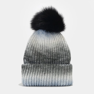Détail d'un bonnet en tricot dégradé avec un pompon noir en fausse fourrure moelleuse