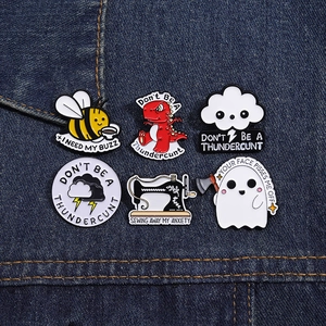 Macro view of assorted cartoon enamel pins featuring a bee, dinosaur, and sewing machine
