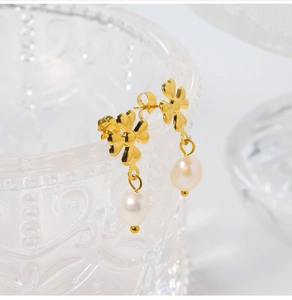 Detail view of golden four-leaf clover earrings with hanging pearls on a glass jar