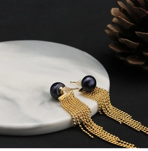 Detail of black pearl earrings with golden chain tassels on white marble surface