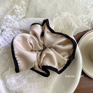 Chouchou géant en soie champagne avec bordure noire présenté dans un plat en porcelaine
