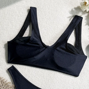 Flat lay of black V-neck bikini top with glossy fabric on textured background