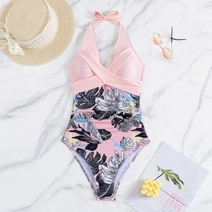 Flat lay of pink halter neck swimsuit with tropical leaf print on marble background
