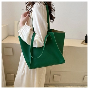 Detailed side view of large green leather tote bag worn by a model in a minimal setting