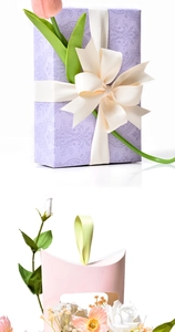 Detail of luxury purple embossed gift box with white ribbon bow and pink tulip flower