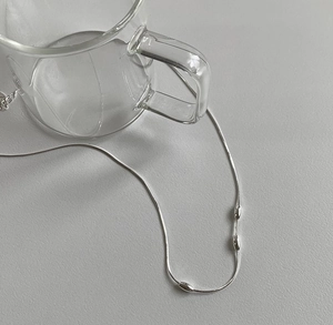 Close-up of silver snake chain necklace with oval beads next to a glass cup