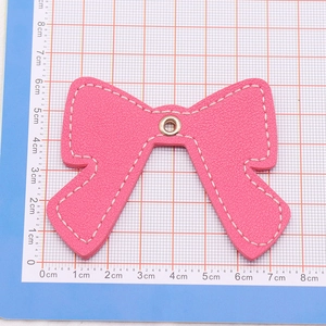 Close-up of a pink leather bow pendant with white stitching and metal eyelet detail